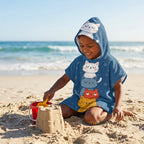 Kind met MiniCat kinderponcho met capuchon op het zand bij zee
