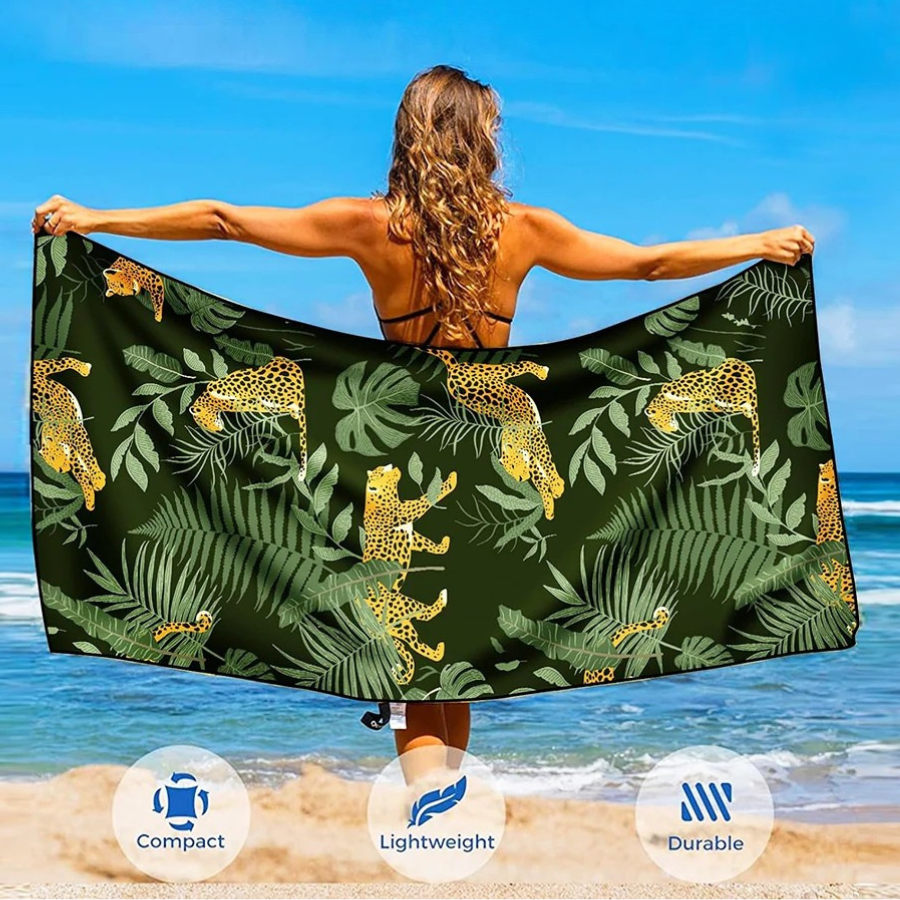 Woman holding rainforest microfibre beach towel open on beach, large quick dry sand free towel