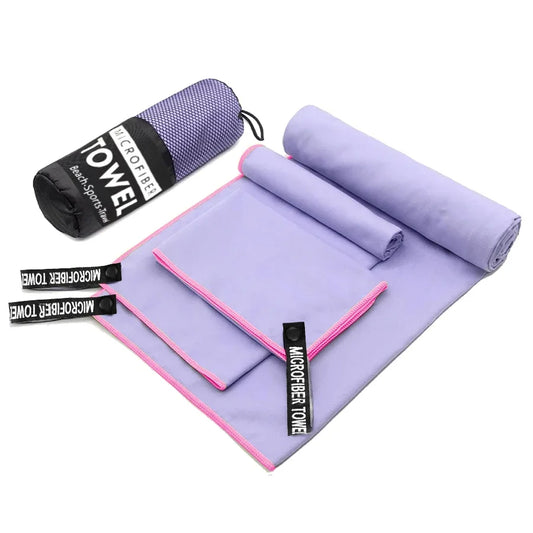 Flat lay of the 3-piece Taro Purple microfibre towel set, showing the small, medium, and large towels unfolded with their pink trim. The compact mesh carry bag is next to the set.