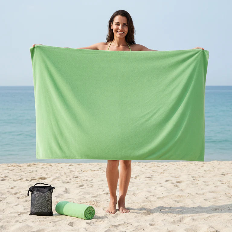 Oversized green microfibre beach towel held by woman on beach, quick dry sand free towel