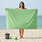 Oversized green microfibre beach towel held by woman on beach, quick dry sand free towel