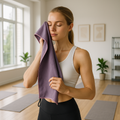 Woman in a bright yoga studio using the small Taro Purple microfibre towel to gently dry her face after a workout.